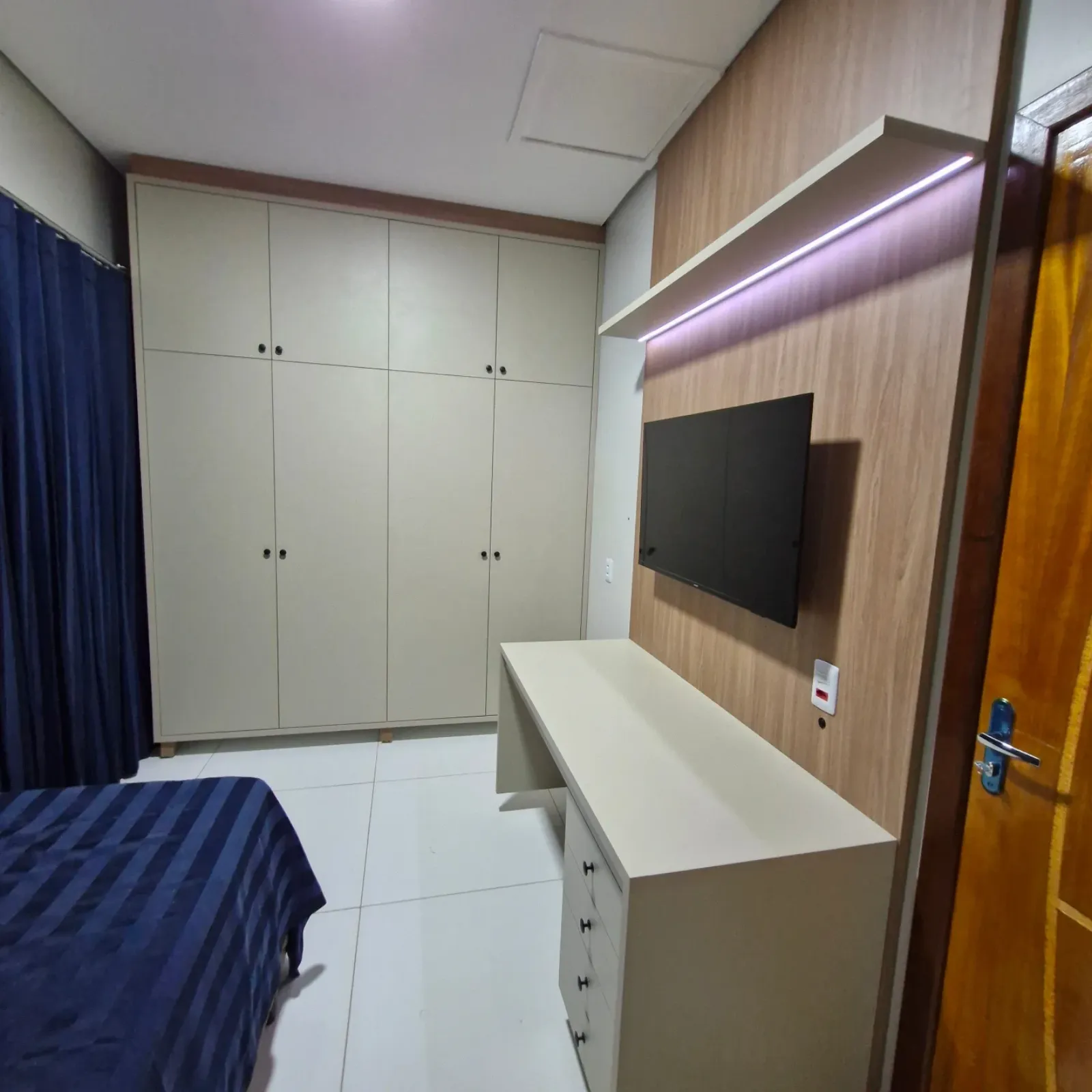 Quarto planejado com guarda-roupa off-white, painel de TV amadeirado e escrivaninha em Primavera do Leste